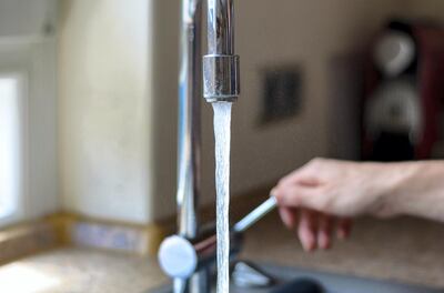 Woman turning on a tap with running water and a chrome faucet indoors in the house, close up of the stream of water
