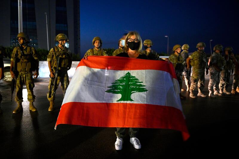 An anti-government protester carries a national flag in front of the Lebanese army soldiers as protesters block the main highway during a protest to demand a change of the sectarian system and finding solutions to the daily-living and economic crisis in Jal El Dib area north of in Beirut.  EPA