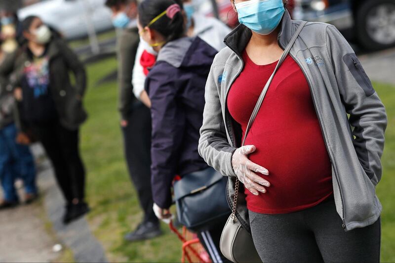 FILE - In this Thursday, May 7, 2020 file photo, a pregnant woman wearing a face mask and gloves holds her belly as she waits in line for groceries with hundreds during a food pantry sponsored by Healthy Waltham for those in need due to the COVID-19 virus outbreak, at St. Mary's Church in Waltham, Mass. A small study in Italy strengthens evidence that pregnant women infected with the coronavirus might be able to spread it to a fetus before birth. Research was released on Thursday, July 9, 2020. (AP Photo/Charles Krupa)