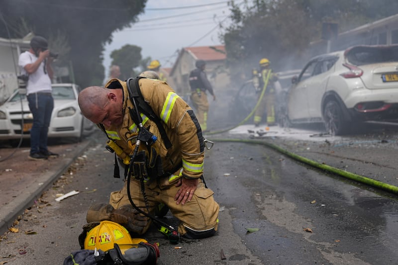 An Israeli firefighter composes himself after he and his colleagues extinguished cars set on fire by a rocket fired from the Gaza Strip in Ashkelon, Israel, on October  9, 2023. AP Photo
