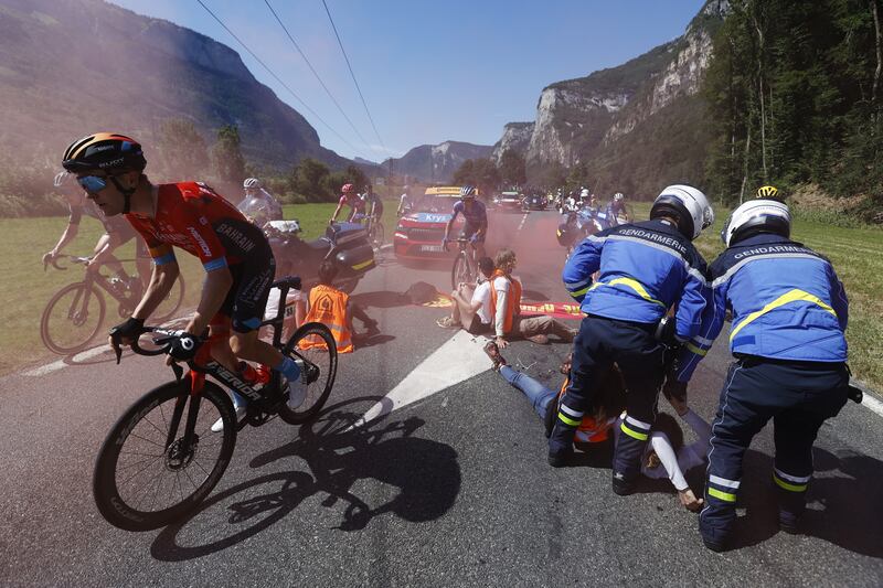 British rider Fred Wright of Bahrain Victorious passes by as police officers try to move protesters sitting on the road during Stage 10 of the Tour de France 2022 on July 12, 2022. EPA