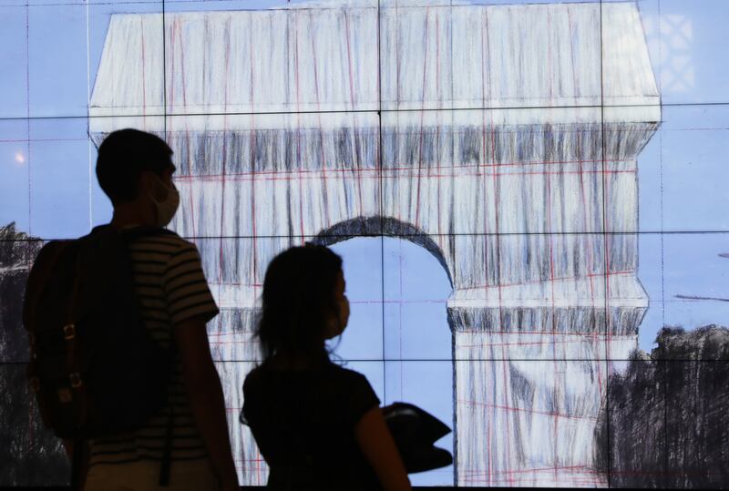 Visitors watch a video on "L'Arc de Triomphe, Wrapped" in Paris, Tuesday, Aug. 24, 2021.  The "L'Arc de Triomphe, Wrapped" project by late artist Christo and Jeanne-Claude will be on view from, Sept. 18 to Oct.  3, 2021.  The famed Paris monument will be wrapped in 25,000 square meters of fabric in silvery blue, and with 3,000 meters of red rope.  (AP Photo / Adrienne Surprenant)
