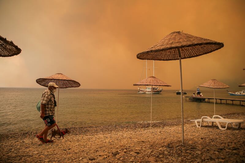 A man walks with his dog on the beach of smoke-engulfed Mazi area as wildfires rolled down the hill toward the seashore, in Bodrum, Mugla.