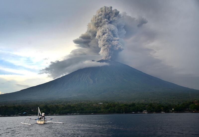A fisherman drives a traditional boat as Mount Agung erupts, as seen from Kubu sub-district in Karangasem Regency on Indonesia's resort island of Bali on November 28, 2017. Sonny Tumbelaka / AFP