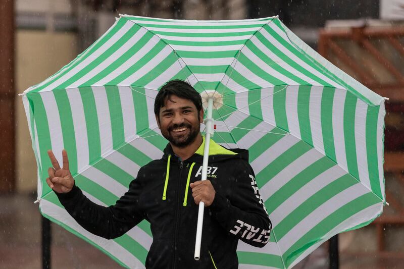 A man stands in the rain, smiling under an umbrella, in Al Quoz, Dubai. Antonie Robertson/The National