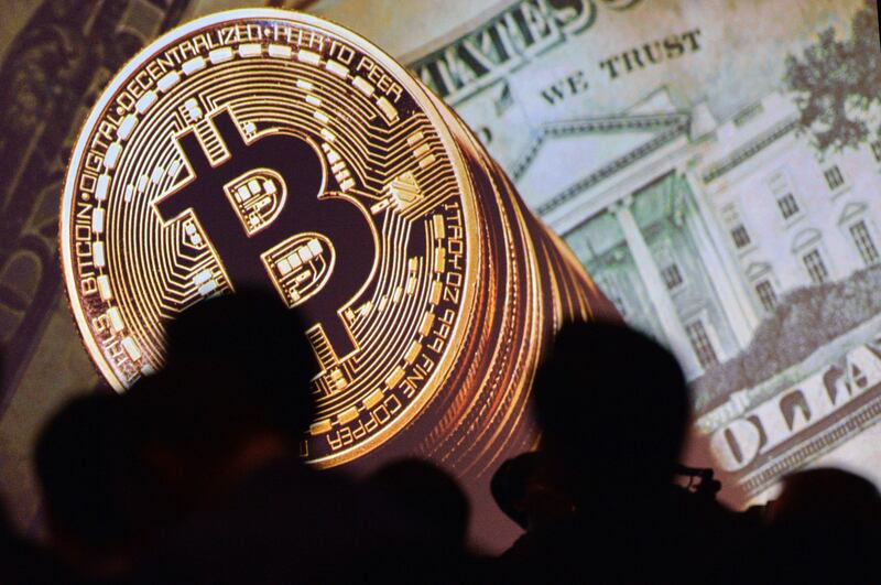 (FILES) This file photo taken on July 04, 2017 shows an image of Bitcoin and US currencies  displayed on a screen as delegates listen to a panel of speakers during the Interpol World Congress in Singapore.
Bitcoin surged through the $5,000 level on October 12, 2017 for the first time since the launch of the unregulated virtual currency more than 8 years ago. / AFP PHOTO / ROSLAN RAHMAN