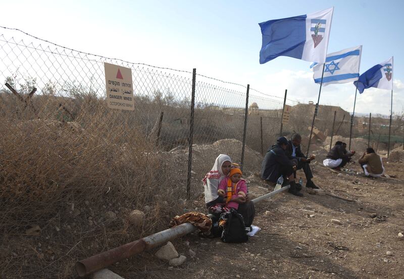 An Ethiopian Orthodox Christian woman sitting with a child by a fence with signs that warn of land mines at the baptismal site known as Qasr Al Yahud, near the West Bank city of Jericho in January 19, 2012.