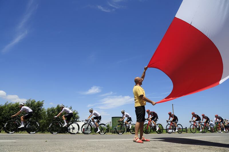 Riders of UAE Team Emirates, left, and INEOS Grenadiers pass a spectator waving a flag during the second stage of the 2024 Tour de France from Cesenatico to Bologna, Italy. EPA