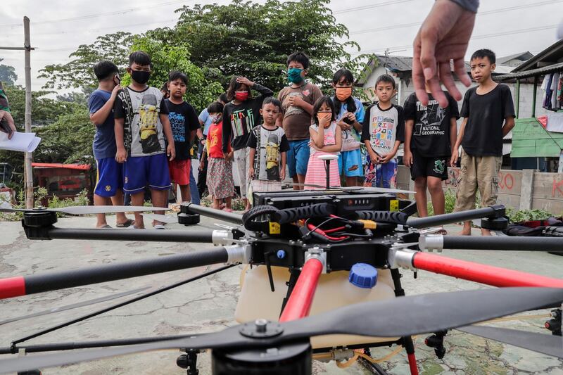 Children wearing protective face masks look at an Indonesian Air Force disinfection drone in a slum area of Jakarta.  EPA