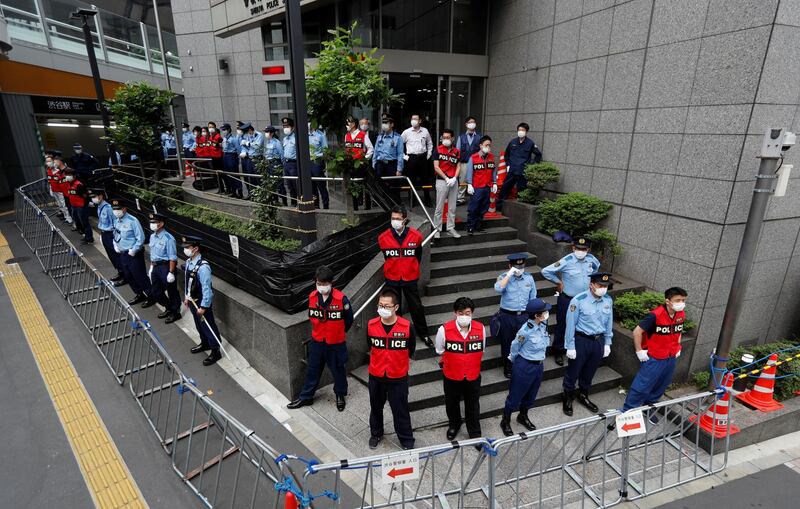 Police officers wearing masks stand guard at the entrance of Shibuya Police Station as demonstrators march in front of them. Reuters