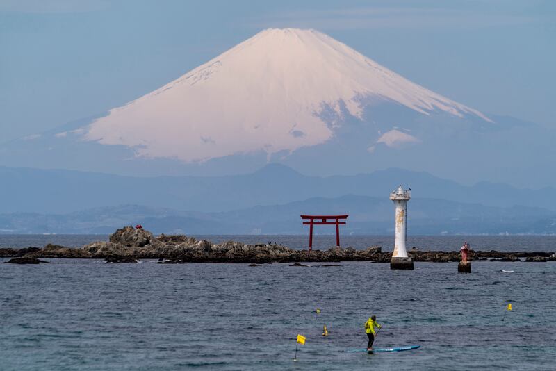 With Mount Fuji in the background, a stand-up paddleboarder cruises near an entrance gate to a Shinto shrine in Sagami Bay, in Zushi, south of Tokyo. AP
