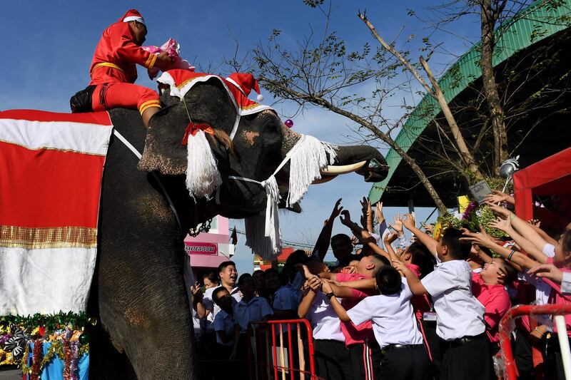 An elephant dressed in a Santa Claus costume with its mahout presents toys and gifts to school children during Christmas celebrations in Ayutthaya. AFP