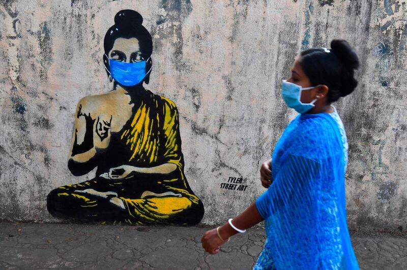 A resident wearing a facemask amid concerns over the spread of the COVID-19 coronavirus walks past a graffiti of Buddha wearing facemask, in Mumbai.  AFP