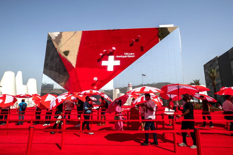 Visitors at the Switzerland Pavilion are given umbrellas to protect themselves from the elements while waiting in line. Victor Besa/The National.