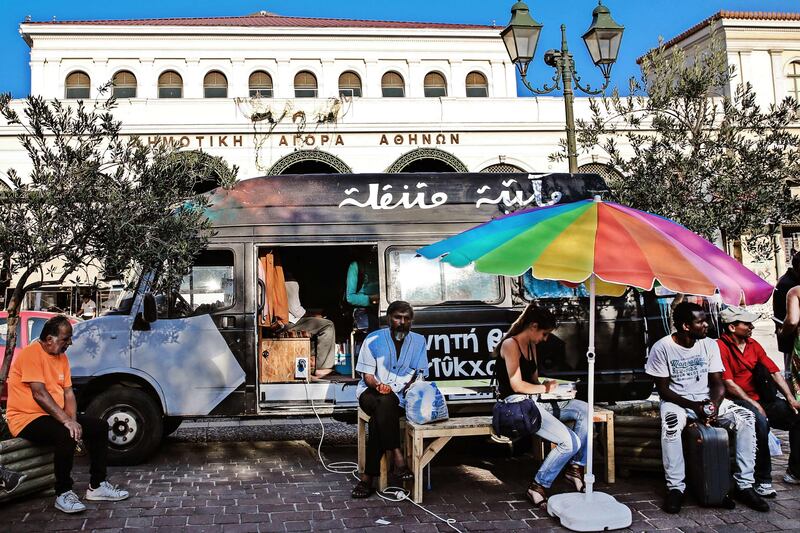 People sit outside a library van in central Athens on August 9, 2017. 
There are increasingly initiatives in Greece to offer reading and books to the tens of thousands of refugees stranded in the country. / AFP PHOTO / LEFTERIS PARTSALIS