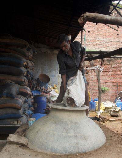 A worker filling a large cauldron with clay for making 'Mitti Attar' or petrichor perfume at a fragrance making unit in Kannauj, India.
