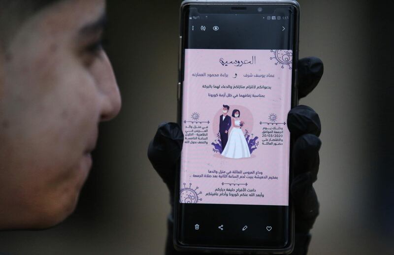 Issam Sharaf, brother of Palestinian groom Imad, holds up a phone showing an electronic image of a wedding invitation with a cartoon of both the bride and groom wearing protective masks, at their home in the village of al-Dahriya, south of Hebron in the West Bank.  AFP