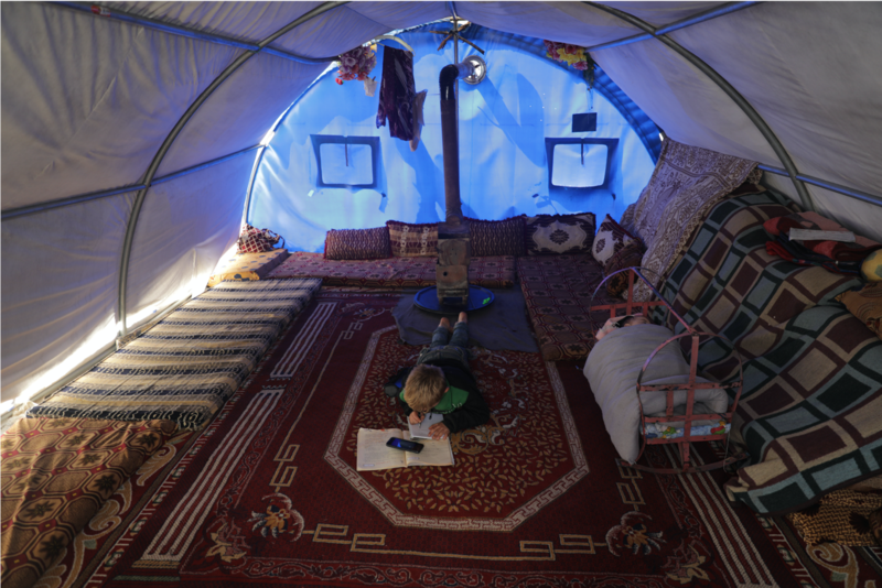 Mahmoud Abdel Hadi, an 8-year old refugee, studies inside his tent after the pandemic forces schools to close. He uses a mobile phone to check instructions for his homework. Photo by Khalil Ashawi