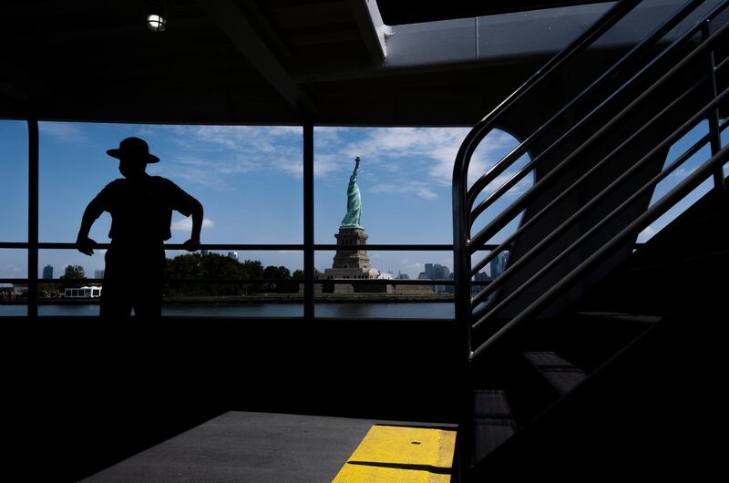 A US National Park Ranger is seen on a ferry with the Statue of Liberty and Liberty Island in the background in New York. EPA