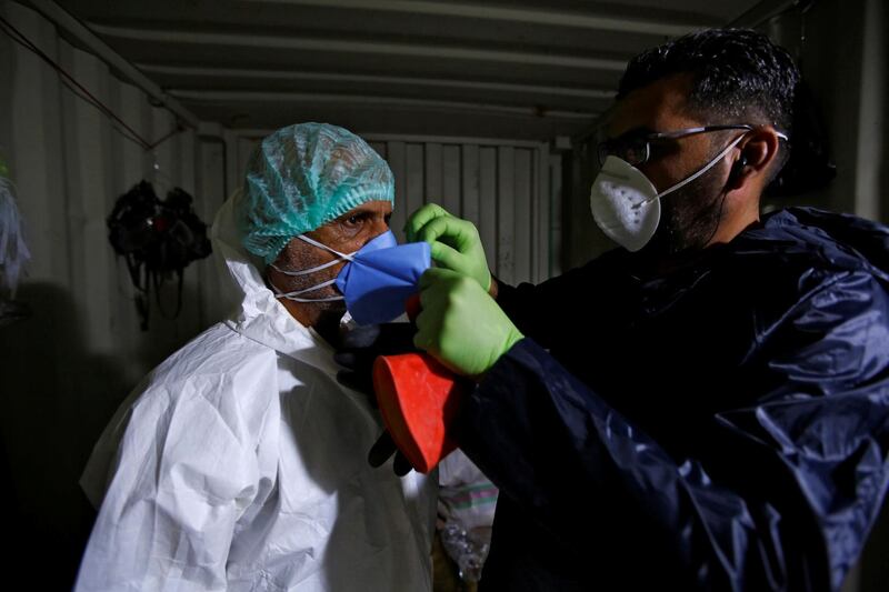 Abdelhussan Kadhim, from the PMF, who volunteered to work in the cemetery, gets help from his fellow to put on his protective mask. REUTERS