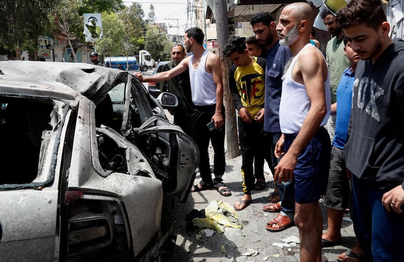 Residents look at a car that was hit in an Israeli air strike, on the main road in Gaza City. Three people who were in the vehicle died. AP