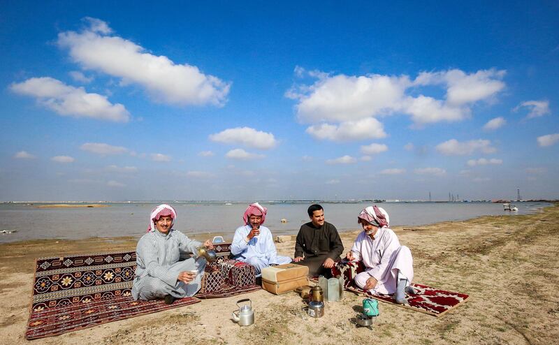 Men have tea together as they rest on mats before a large rainwater flooding pool in al-Rawdatayn, about 115 kilometres north of Kuwait City, on December 18, 2019. - Heavy rains that hit Kuwait in recent days have damaged camps across the country's desert where camping is popular during the the winter and spring season. (Photo by YASSER AL-ZAYYAT / AFP)