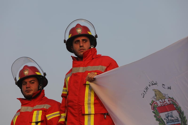 Firefighters hold a flag as they commemorate a month since Beirut's deadly explosion. Getty Images