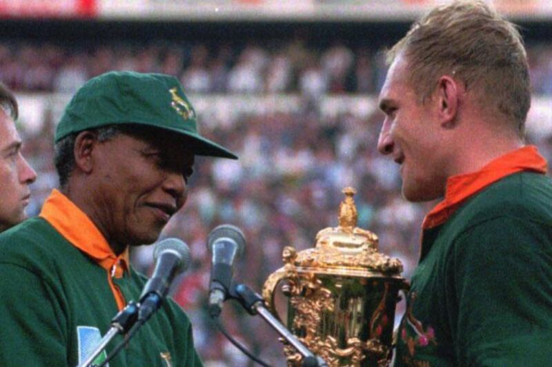 South African rugby captain Francios Pienaar, right, receives the Rugby World Cup trophy from President Nelson Mandela, left, who wears a South African rugby shirt, after South Africa defeated New Zealand in Johannesburg, in this June 1995 photo.