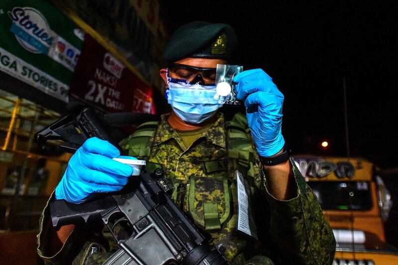 On of the troops deployed to enforce the lockdown in Metro Manila holds up a sachet containing a 'holy host' - the wafer used for the Christian sacrament of Holy Communion.  AFP