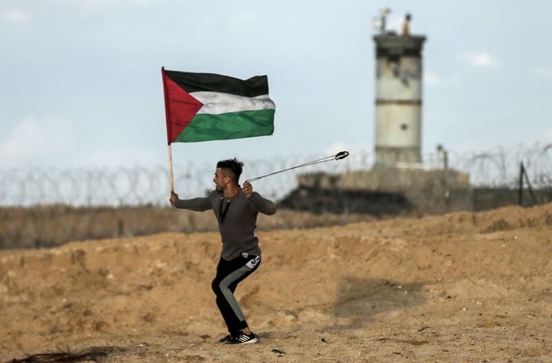 A masked Palestinian protester carries a national flag as he hurls stones during a demonstration calling for an end to the Israeli blockade on Gaza, on a beach in Beit Lahia near the maritime border with Israel, on November 5, 2018. / AFP / MAHMUD HAMS
