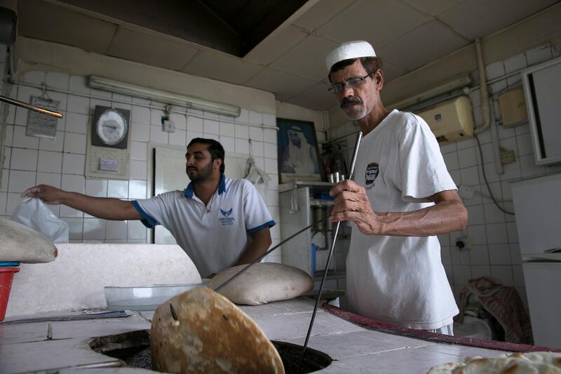ABU DHABI, UNITED ARAB EMIRATES, May 5, 2015:  
(R) Kashmiri baker Ghulam Fareed, 51, prepares fresh flat bread for a customer as he and his assistant work away a hot Spring afternoon at his brother's bakery, the Mohammed Murid Abdul Karim bakery in central Abu Dhabi. (Silvia Razgova / The National)  (Usage: May 5, 2015, Section: RV, Reporter: Zaineb al Hassani *** Local Caption ***  SR-150505-bakeries08.jpg