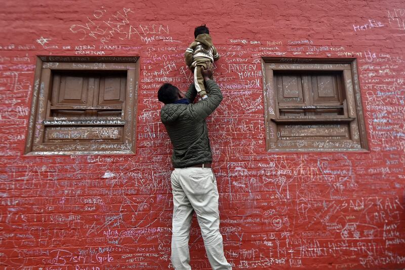 A child helped by his father writes a message on the wall at the Saraswati temple for the Hindu festival of Basant Panchami, in Kathmandu. AFP
