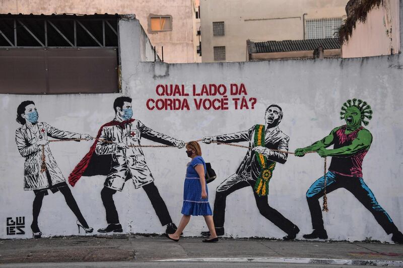 A woman passes by a graffiti depicting Brazilian President Jair Bolsonaro and a figure representing the novel coronavirus pulling a rope against health workers with the question "Which side of the rope are you on?" in Sao Paulo, Brazil. AFP