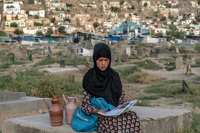 Sara, a 14-year-old, an Afghan girl, sits on a grave and reads a book as she sells water at a cemetery in Kabul, Afghanistan. AP