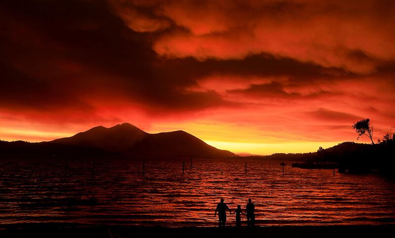 Evacuees from Lucerne, from left, Ken Bennett with Ember Reynolds, 8, and Lisa Reynolds watch the sunset as smoke from the Ranch Fire rises into the sky at Austin Park Beach in California's Clearlake with Mount Konocti in the background. (Kent Porter/The Press Democrat via AP)