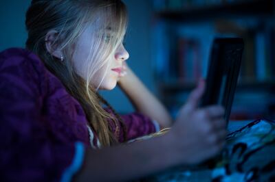 Beautiful long haired teenager girl reading from tablet, in the dark room at night in the bed, with her face illuminated by the screen. Getty Images