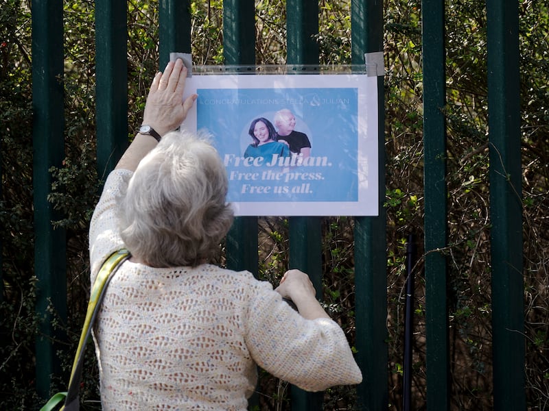 A supporter of Julian Assange fixes a sign to a wall outside Belmarsh Prison. PA