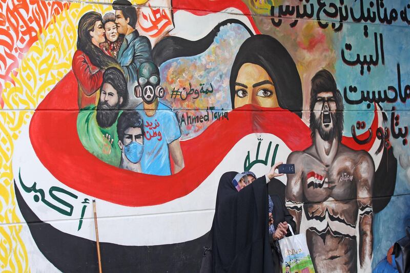 Iraqi women take selfies in front of a mural during ongoing anti-government protests in Tahrir square. AFP