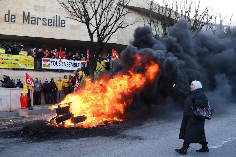 A prison visitor raises her fist walking past a fire supporting the strike of prison guards (background) demonstrating outside the Baumettes prison in Marseille, as part of a nationwide movement to call for better safety and wages. Anne-Christine Poujoulat / AFP