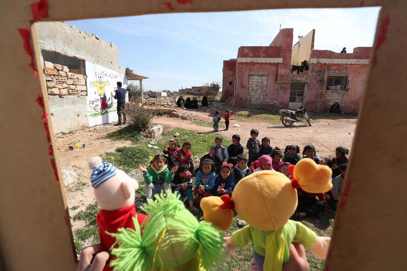Syrian children watch a puppet show performed by a local theatre group amidst the ruins of buildings destroyed during Syria's civil war, in al-Fua, in the country's northwestern Idlib province on March 30, 2021.  / AFP / OMAR HAJ KADOUR
