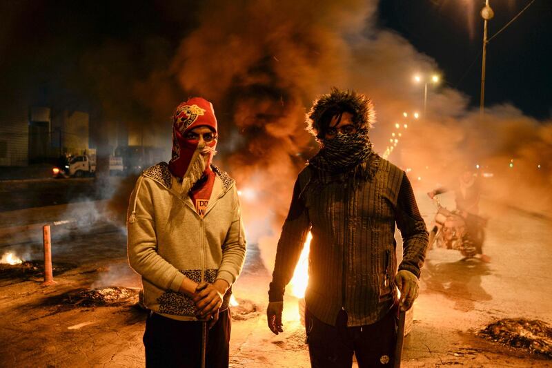 Masked anti-government protester stand before flaming tyres at a make-shift roadblock in the central Iraqi holy shrine city of Najaf.  AFP