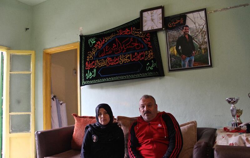 The parents of 26-year-old Hussein Shinawi sit beneath his portrait in their apartment in the Hizbollah-controlled neighbourhood of Burj Al Barajneh. Josh Wood for The National.

