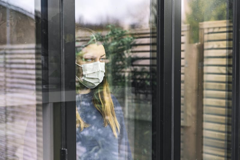 A woman looking through window with mask - stock photo. Getty Images