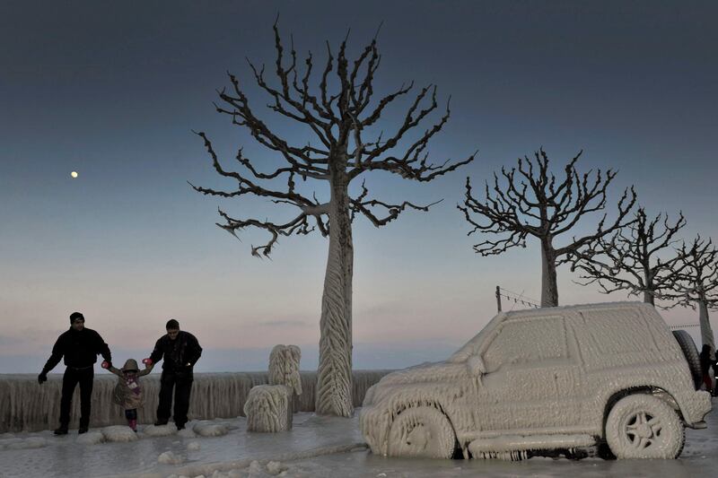 People walk along an icy promenade past ice covered cars and trees on the shores of Lake Geneva in Versoix, Switzerland, Sunday, Feb.  5, 2012. Across Eastern Europe, thousands of people continued to dig out from heavy snow that has fallen during a cold snap that struck more than a week ago and has killed hundreds of people. (AP Photo/Keystone/Martial Trezzini) *** Local Caption ***  APTOPIX Switzerland Europe Weather.JPEG-004e5.jpg