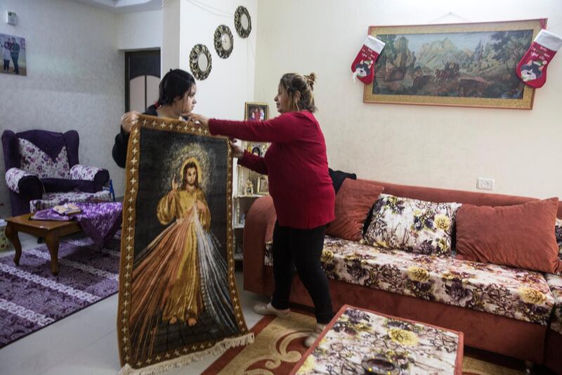 May Ayyad, 26, and her mother Siham ,55, as they try to decide where to hang a carpet showing a woven picture of Jesus Christ that was given to her family by a priest . May has received a permit to travel to Bethlehem with her husband, but they were worried his salary wouldnÕt arrive in time to pay for the trip. Ayyad dreams of making it to Paris: she has an Eiffel Tower in her apartment, which she had now adorned with a Santa hat. (Photo by Heidi Levine for The National).