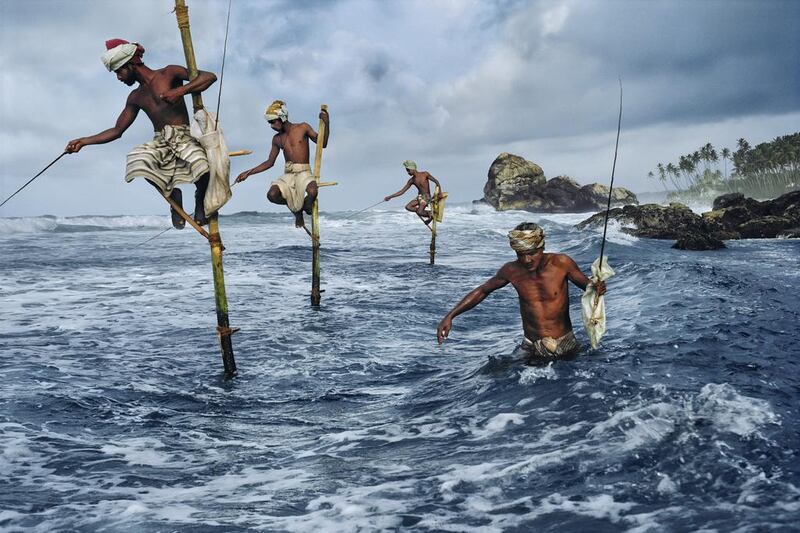 Clad in traditional saram, a group of men fish using wooden perches at Sri Lanka’s south coast. They were said to use such poles to be able to poach in shallow waters without disturbing the fish. Weligama, Sri Lanka, 1995.