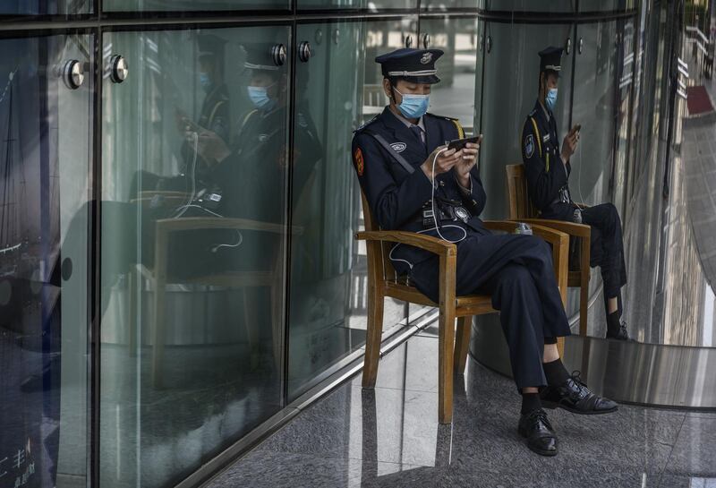 A Chinese security guard  wears a  protective mask as he watches a program on his mobile phone outside an office building in Beijing. Getty Images