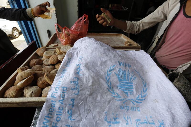 epa07660933 A man (R) displays bread, covered with a sack of the World Food Program (WFP), for sale at a bakery in Sana'a, Yemen, 20 June 2019. According to reports, WFP has threatened to suspend aid deliveries to Houthi-controlled areas of Yemen if the organization is not allowed to reach the most vulnerable people, accusing the Houthis of manipulating food assistance. The WFP delivers monthly rations or cash to 10.2 million people of Yemen's 26-million population.  EPA/YAHYA ARHAB