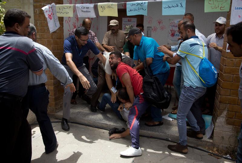 Palestinians prevent an UNWRA employee form setting himself on fire employee sits during a protest at the United Nations agency for Palestinian refugees (UNRWA) headquarters in Gaza City on Wednesday, July 25, 2018. UNWRA staff are protesting the agency's decision to fire dozens of Palestinian staff in Gaza in the Gaza Strip. (AP Photo/Khalil Hamra)