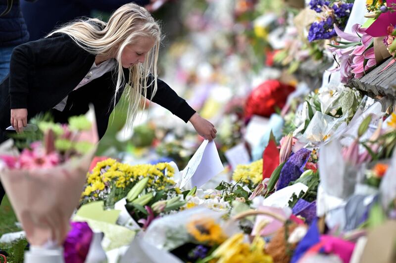 A young girl places a note among flowers left in tribute to victims in Christchurch, on March 17, 2019, two days after a shooting incident at two mosques in the city. A right-wing extremist has been charged in the horrifying gun attacks on two New Zealand mosques, which left 49 people dead and dozens more injured. / AFP / Anthony WALLACE
